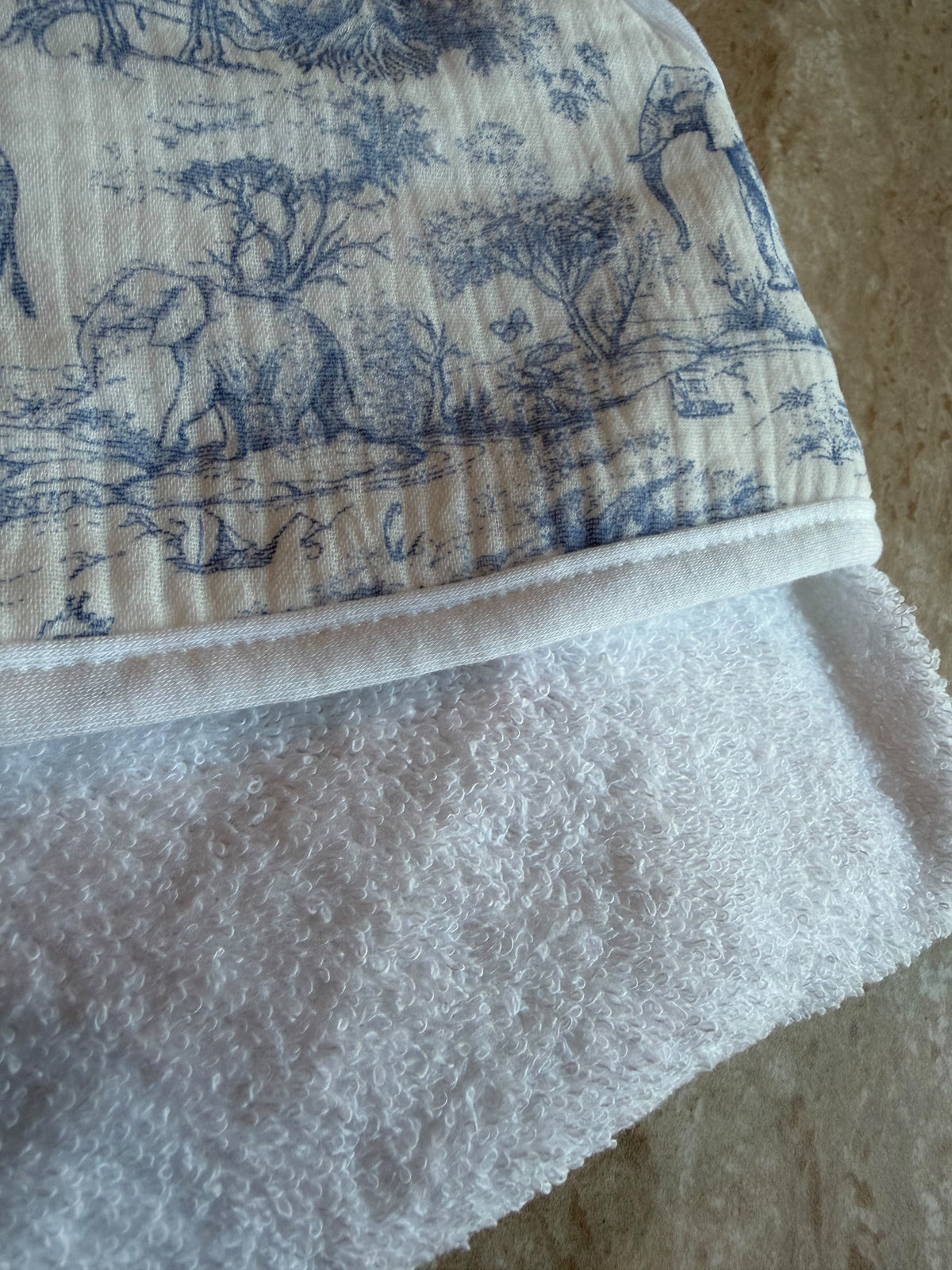 Gros plan sur la capuche en toile de Jouy bleue et l'éponge blanche de la cape de bain Safari