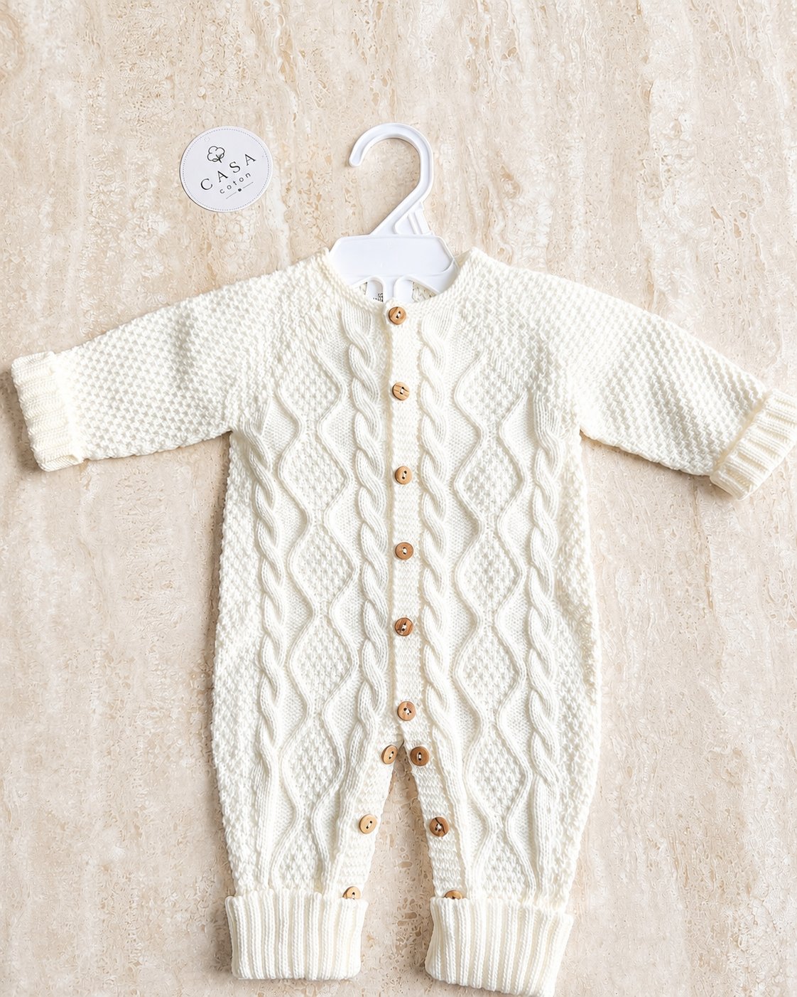 Combinaison bébé Noa en maille blanche à torsades, présentée à plat