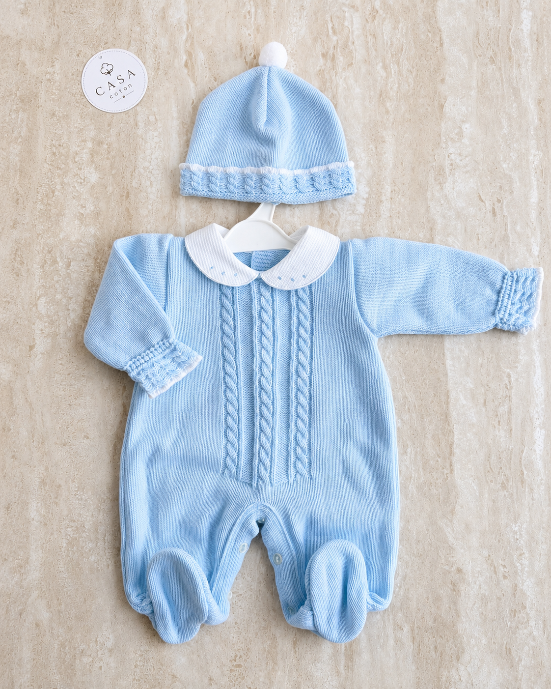 Combinaison et bonnet bébé Nilo en maille bleu ciel, présentés à plat