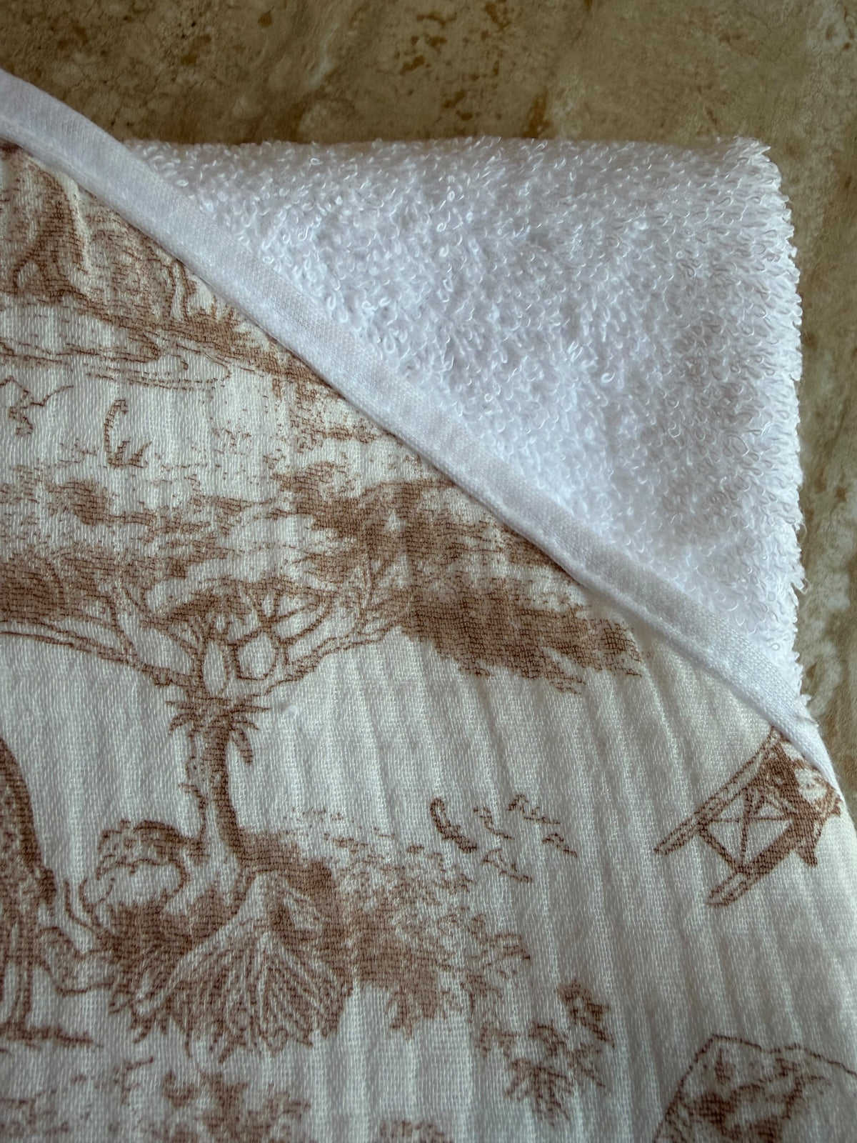 Gros plan sur la capuche en toile de Jouy beige et l'éponge blanche de la cape de bain Safari