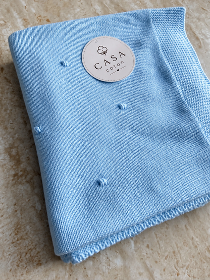 Grande couverture bébé Léo en maille popcorn bleu clair, dépliée avec son étiquette Casa Coton