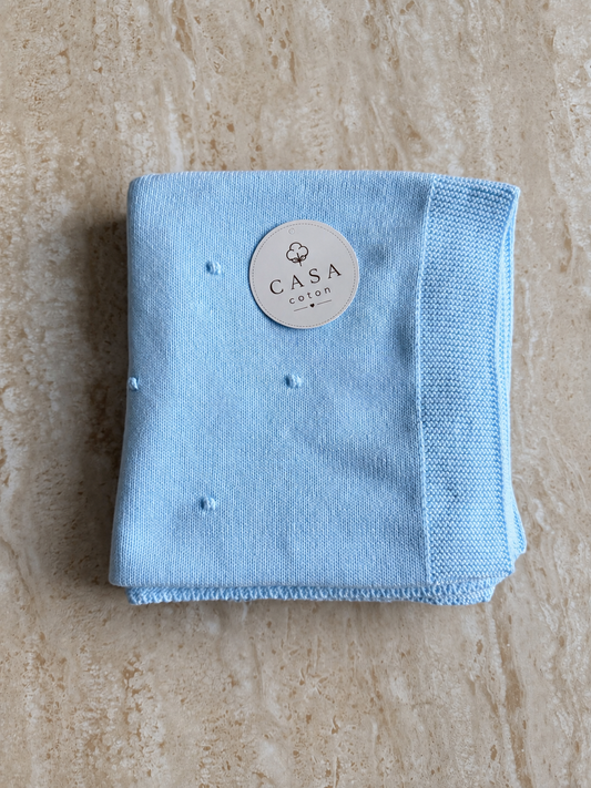 Grande couverture bébé Léo en maille popcorn bleu clair, pliée avec son étiquette Casa Coton