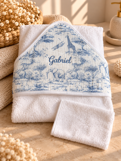 Cape de bain Safari en toile de Jouy bleue, posée à plat avec son gant de toilette